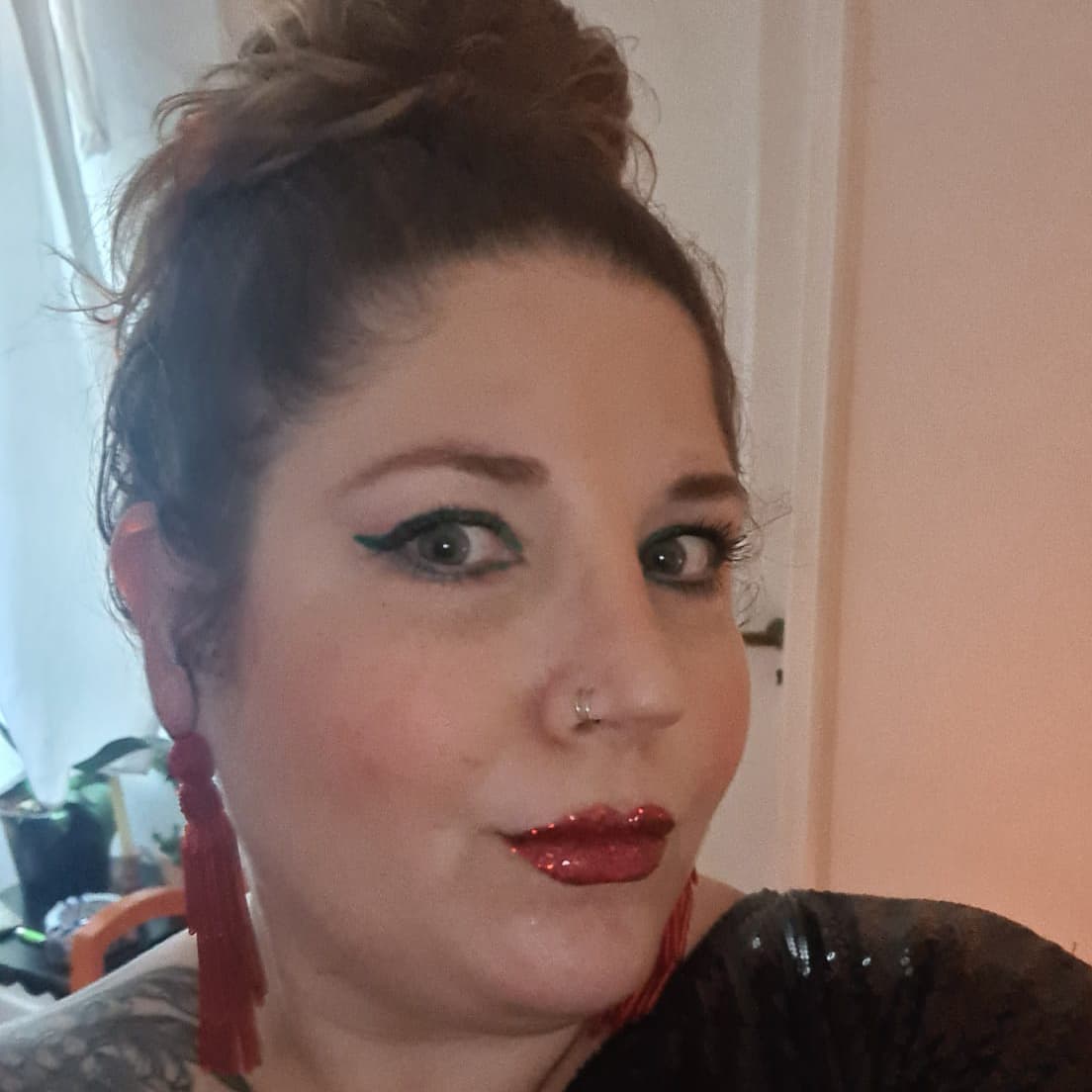 Foto de Julia Fernandez, uma mulher branca com piercing no nariz, vestindo um batom vermelho brilhante e maquiagem sobre os olhos verdes